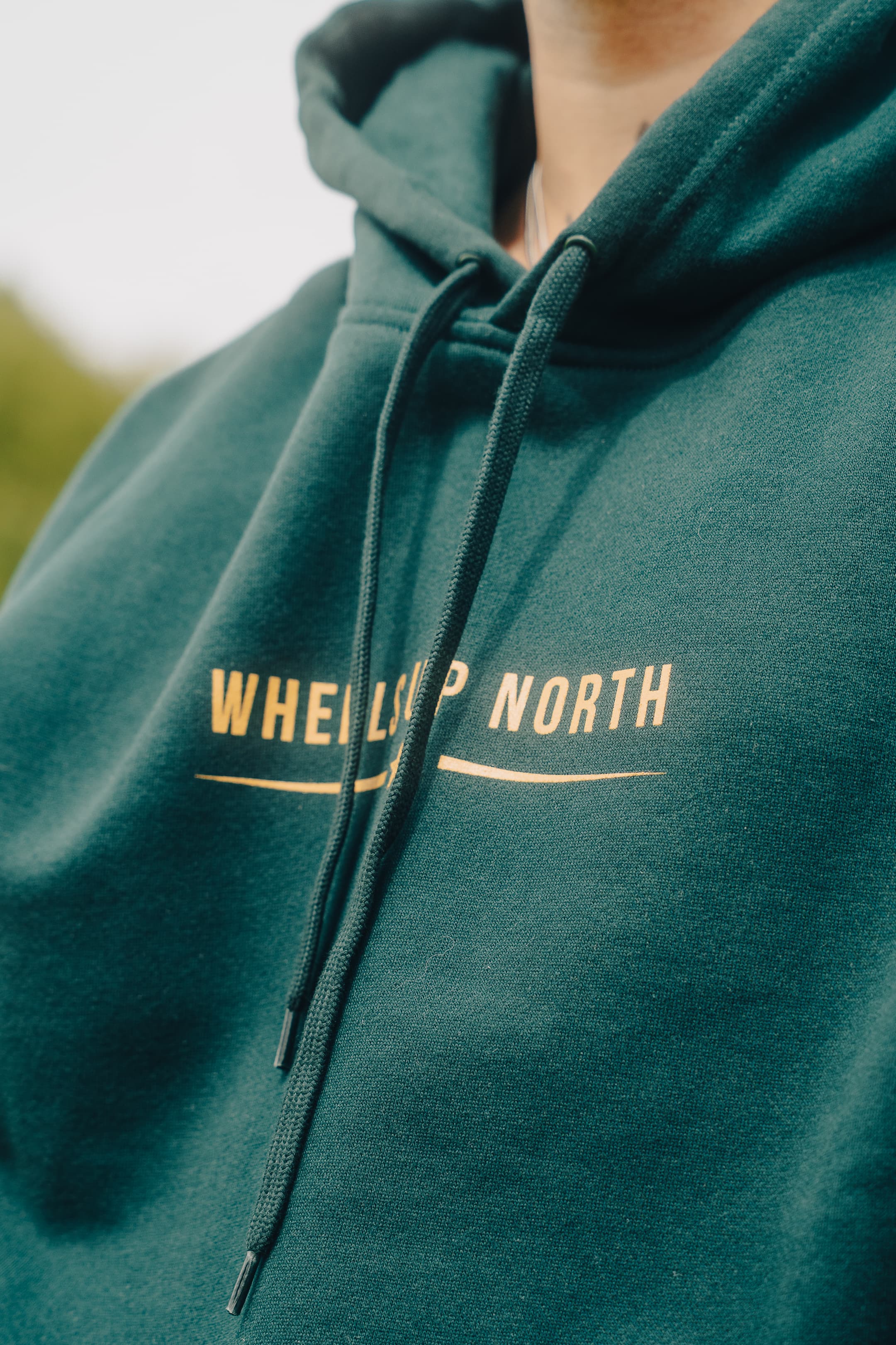Grass 'Routes' Hoodie - Green - close-up of the gold wheels up north chest logo on the green hoodie
